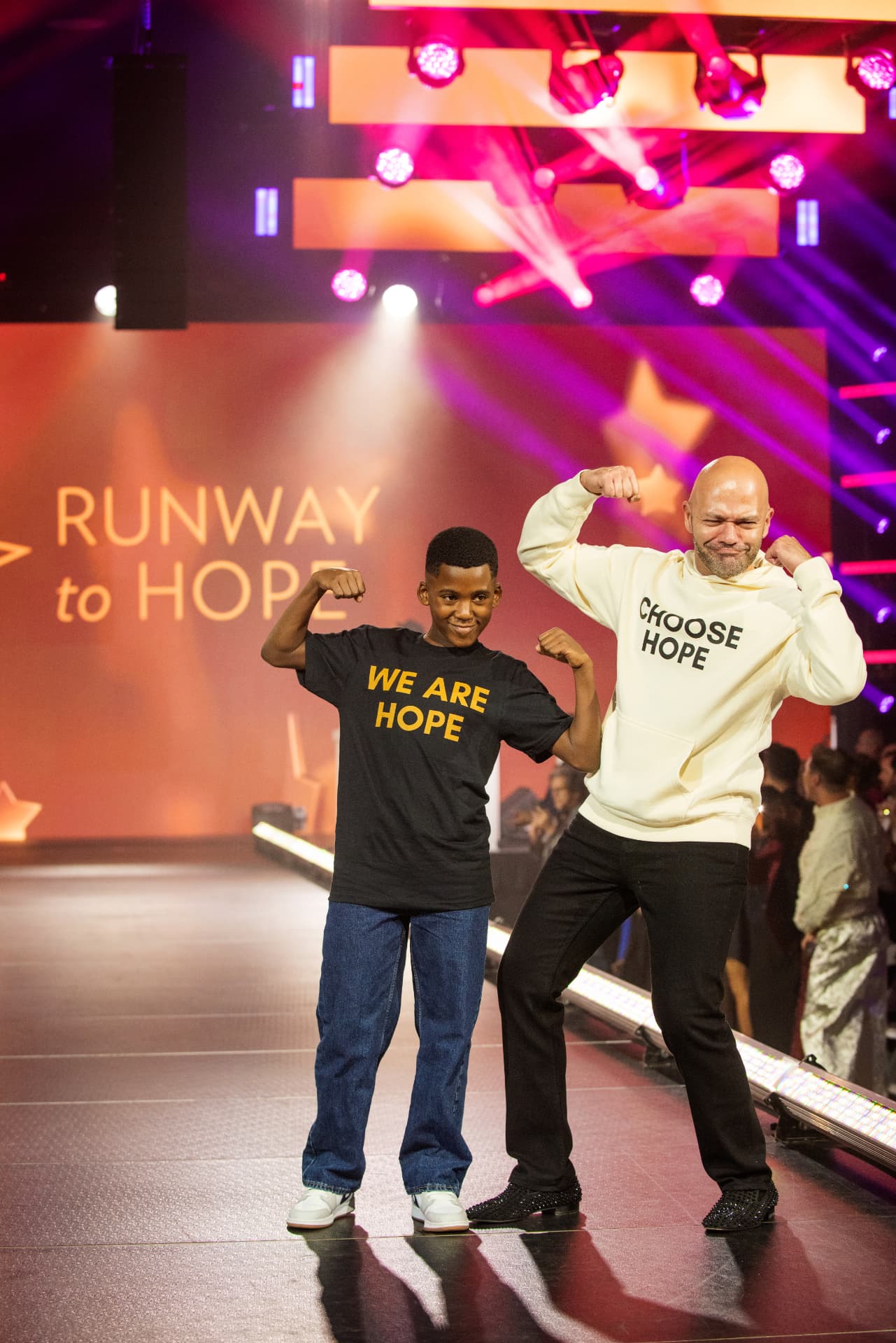 Young walker and host flexing in We Are Hope and Choose Hope shirts during the Runway to Hope moment on the runway