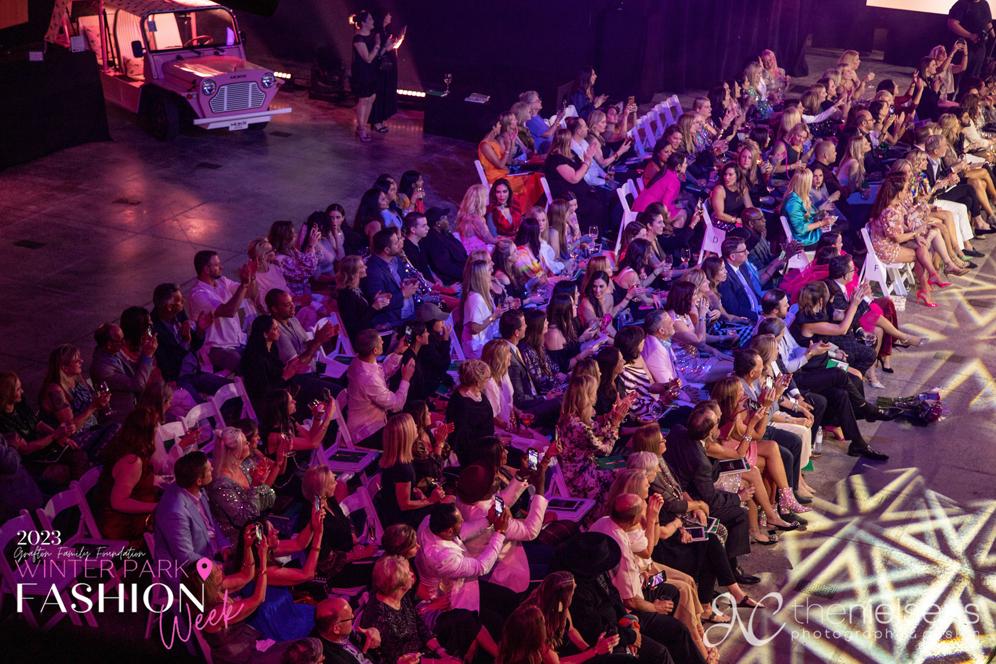 Guests applauding from the venue floor, a pastel pink Moke parked alongside