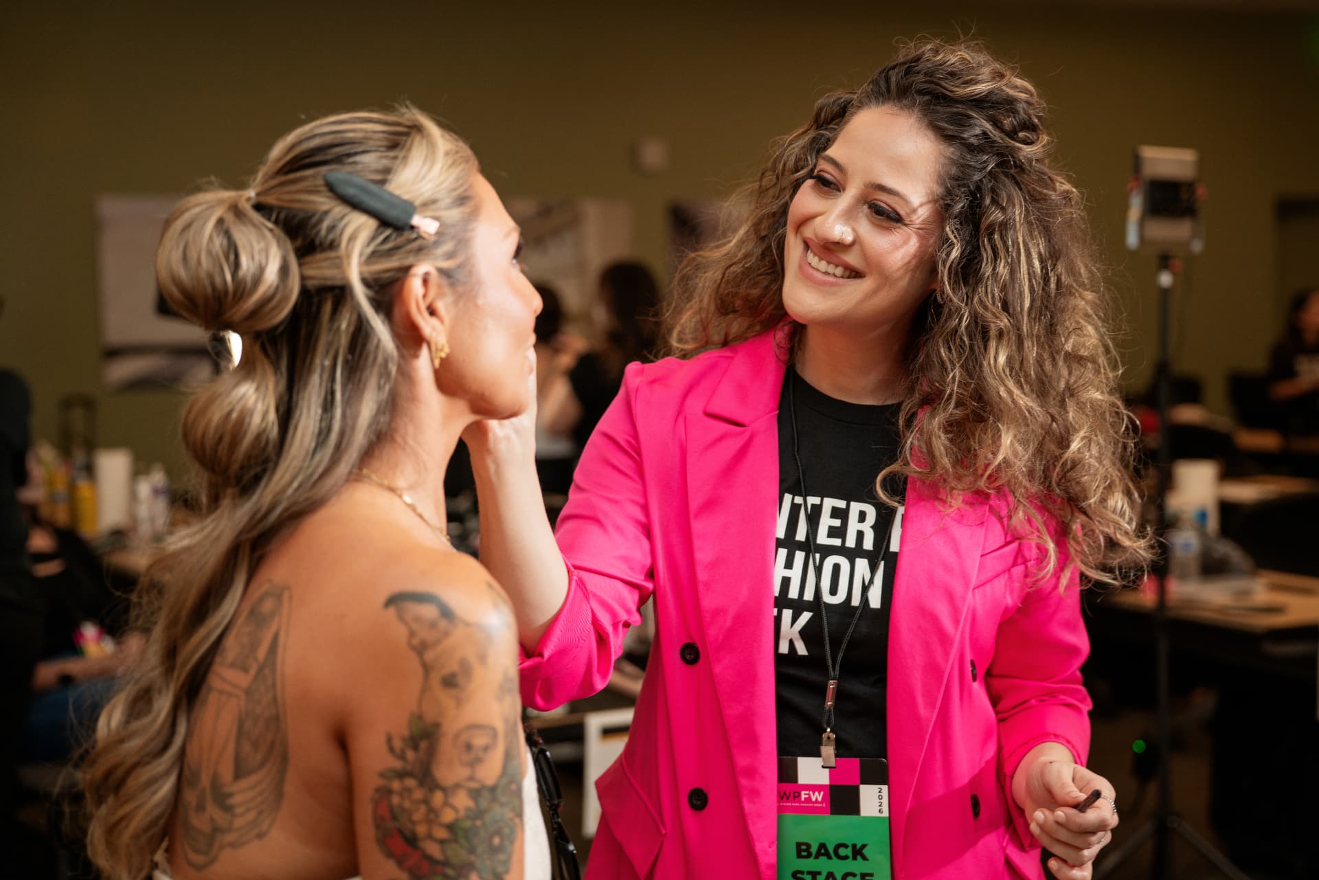 Backstage team member in a hot-pink blazer laughing with a model during hair and makeup