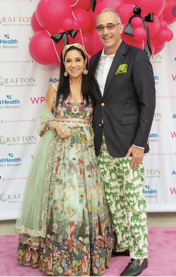 Couple in an embroidered lehenga and printed trousers posing beneath the pink balloon arch