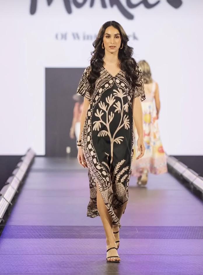 Model in a black and tan patterned dress and hoop earrings walking the runway for Monkee's of Winter Park