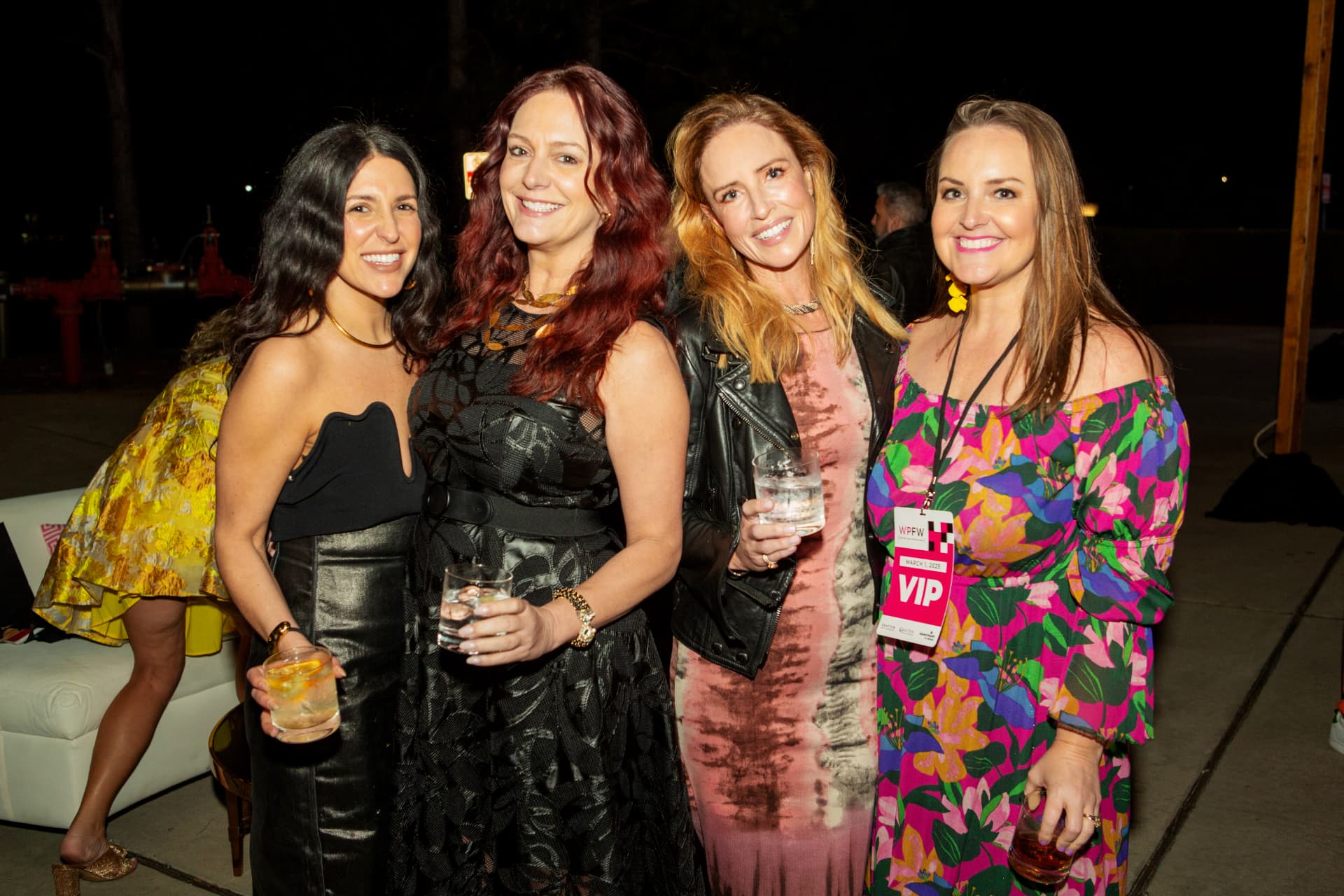 Four guests posing with drinks at an outdoor evening reception