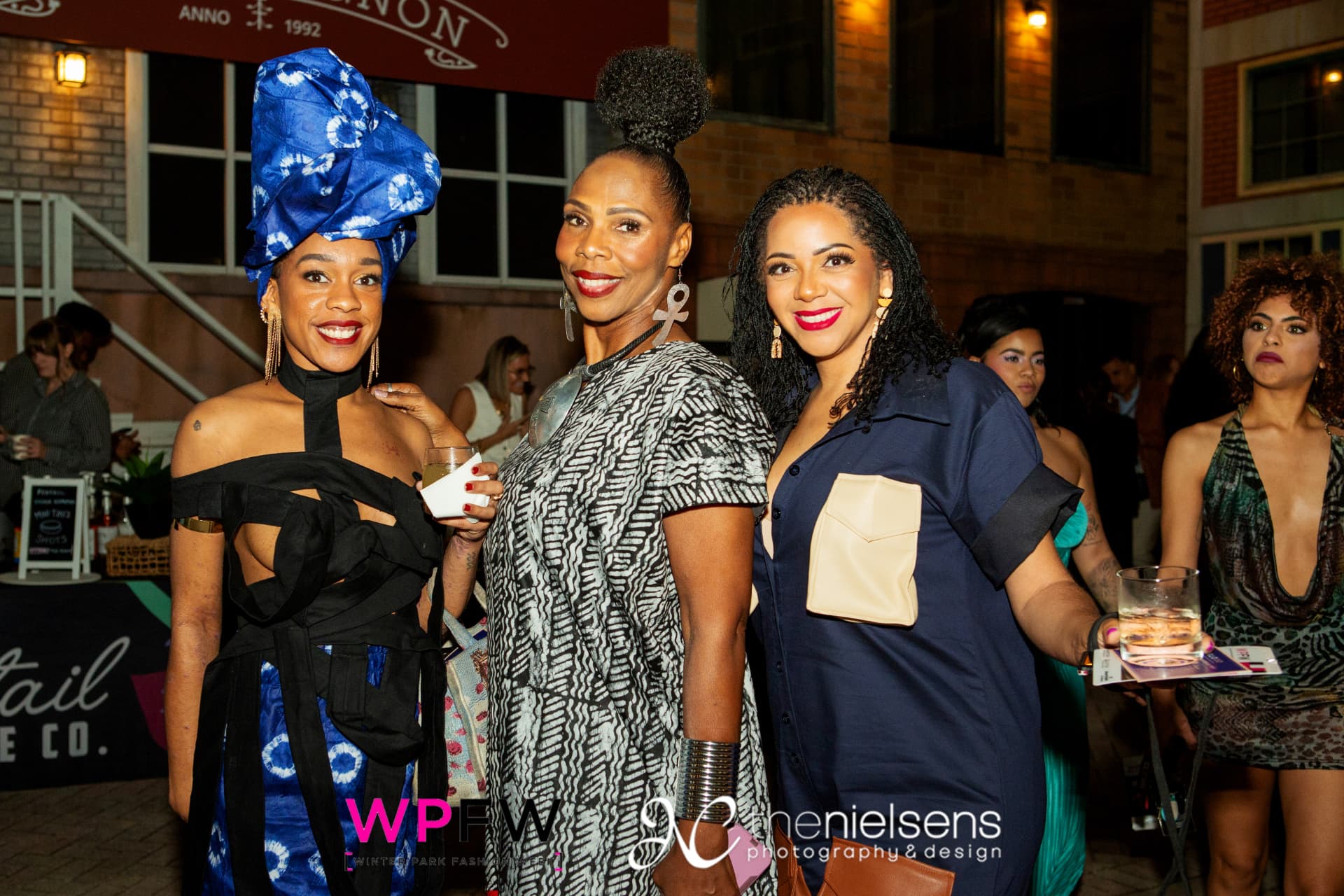Three guests posing with drinks outside the venue at night
