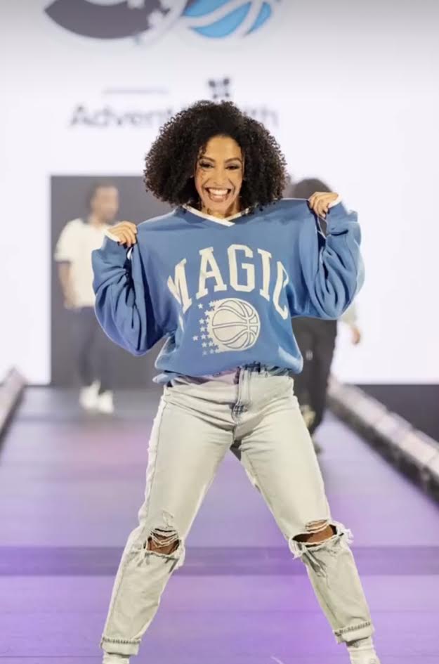 Model in a blue basketball-print sweatshirt, light-wash jeans and white sneakers walking the runway