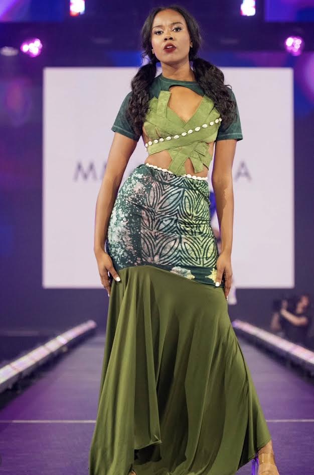 Model in a green two-piece with a cowrie-shell belt on the runway